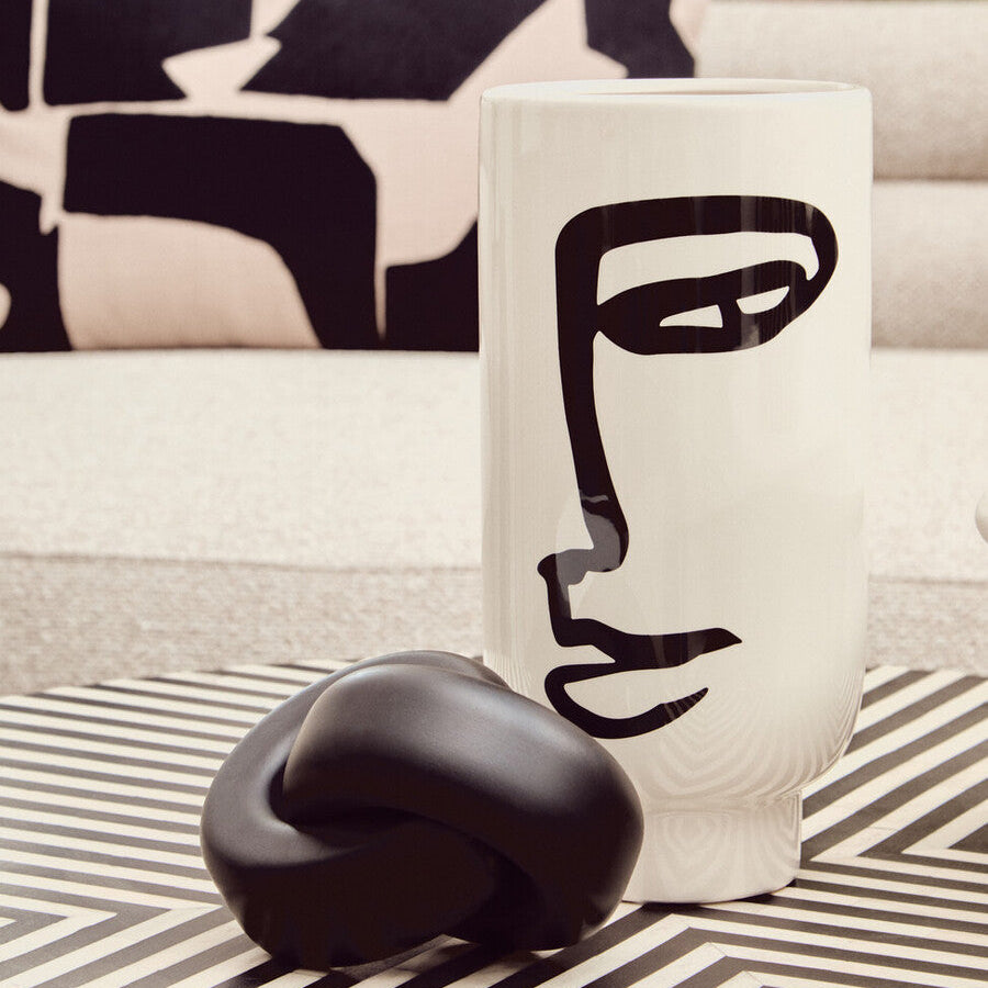 Decorative vase with abstract face design on a striped surface