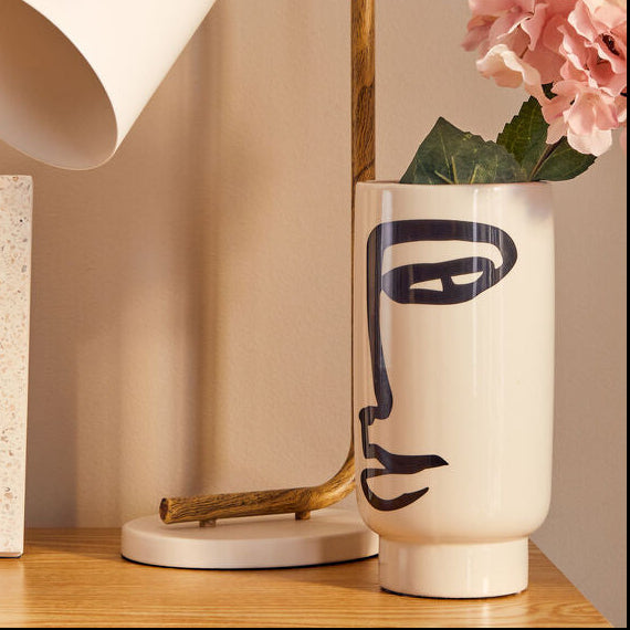 Small desk lamp, photo frame, and vase with flowers on a wooden surface.
