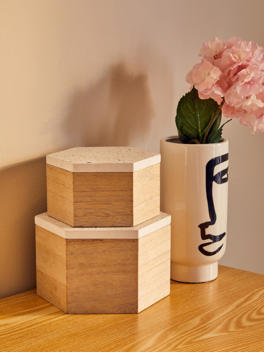 Two wooden hexagonal boxes and a vase with pink flowers on a wooden surface.