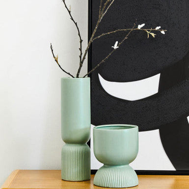 Two green vases on a wooden surface with a black and white abstract artwork in the background.