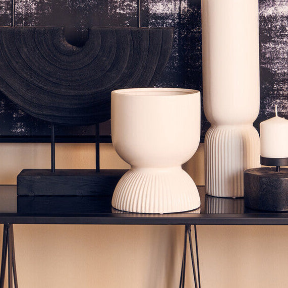 Decorative setting with vases, candles, and a plant against a textured wall.