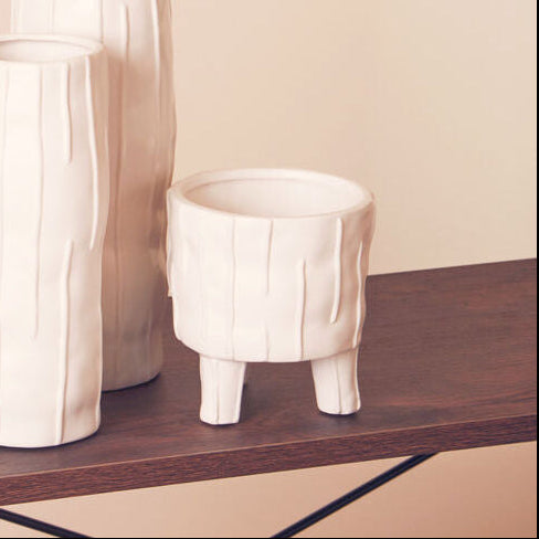 Two white ceramic vases on a wooden shelf with a beige background
