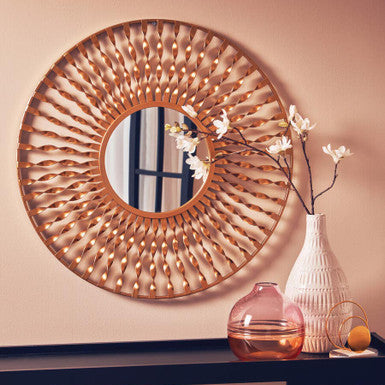 Decorative round mirror with wicker frame on a wall above a shelf with vases.