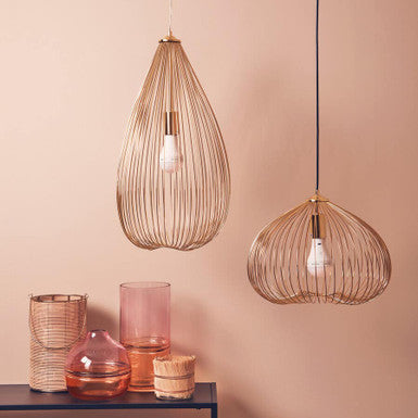Two wire pendant lights hanging against a pink wall with decorative vases on a table.