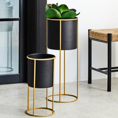 Two black planters with gold stands in a room setting.