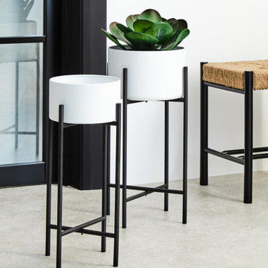 Two white planters with black stands on a light wood floor.