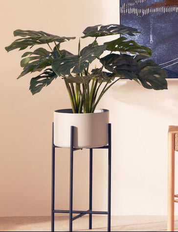 Abstract art piece on a wall with a plant and bench in the foreground