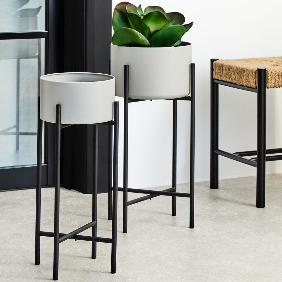 Two modern planters with black stands on a light-colored floor.