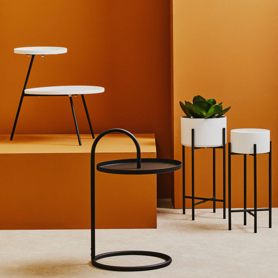 Modern black and white side tables against a warm orange wall.