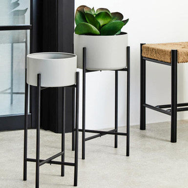 Two white planters with black stands on a light-colored floor.