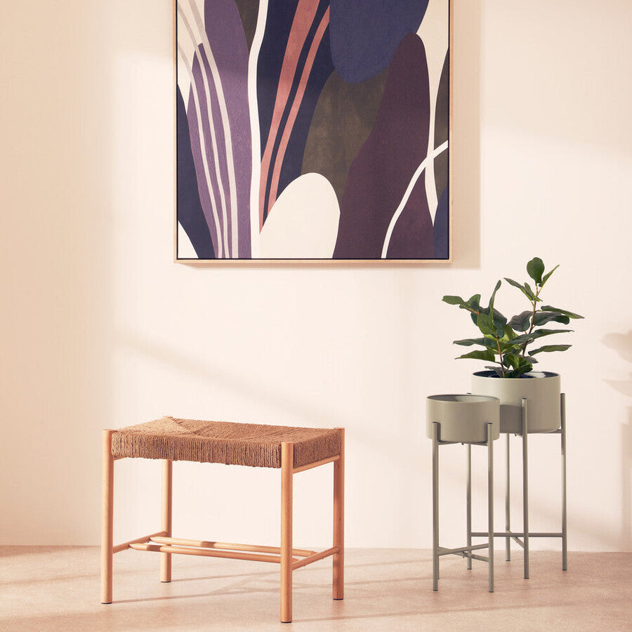 Abstract art piece on a wall with a small table and plant in the foreground.