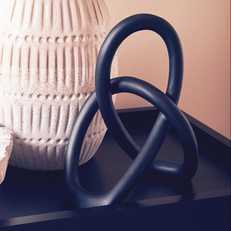 Decorative navy blue sculpture on a dark surface with a textured white vase in the background.