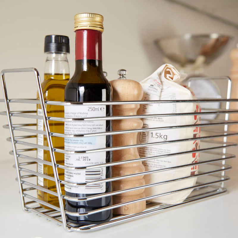 Metal kitchen storage basket with various items on a countertop