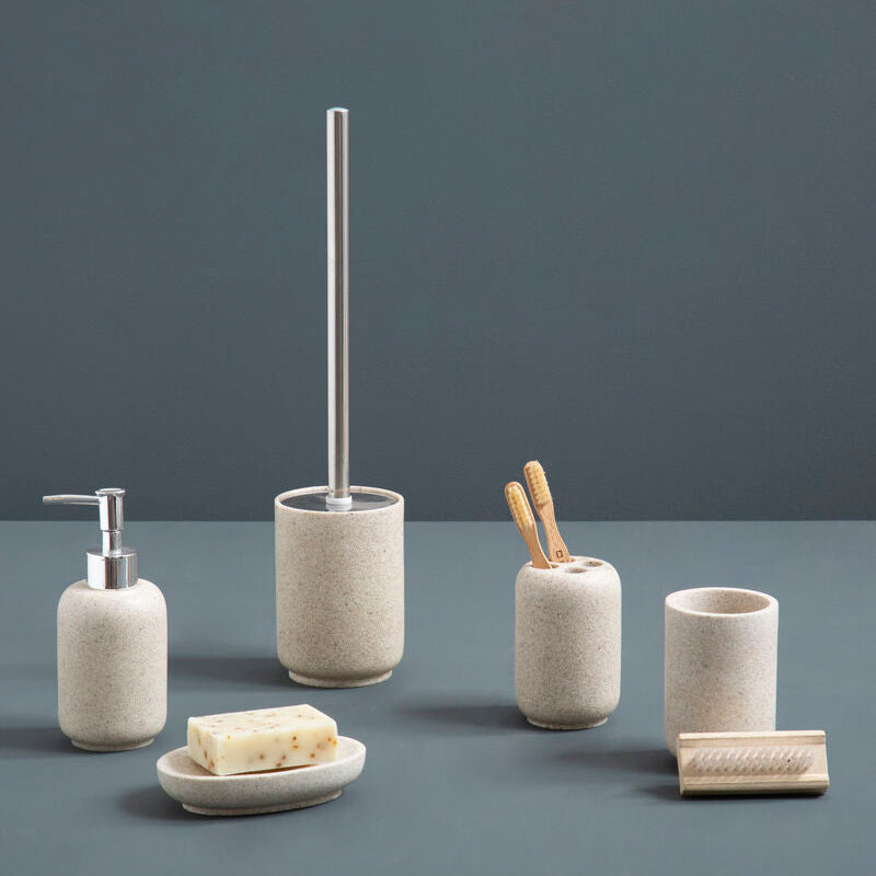 Set of bathroom accessories including a soap dispenser, toilet brush holder, and other items on a gray surface with a dark gray background.