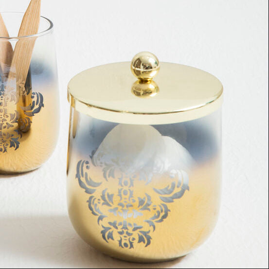 Two gold toothbrush holders with decorative lids on a white surface.