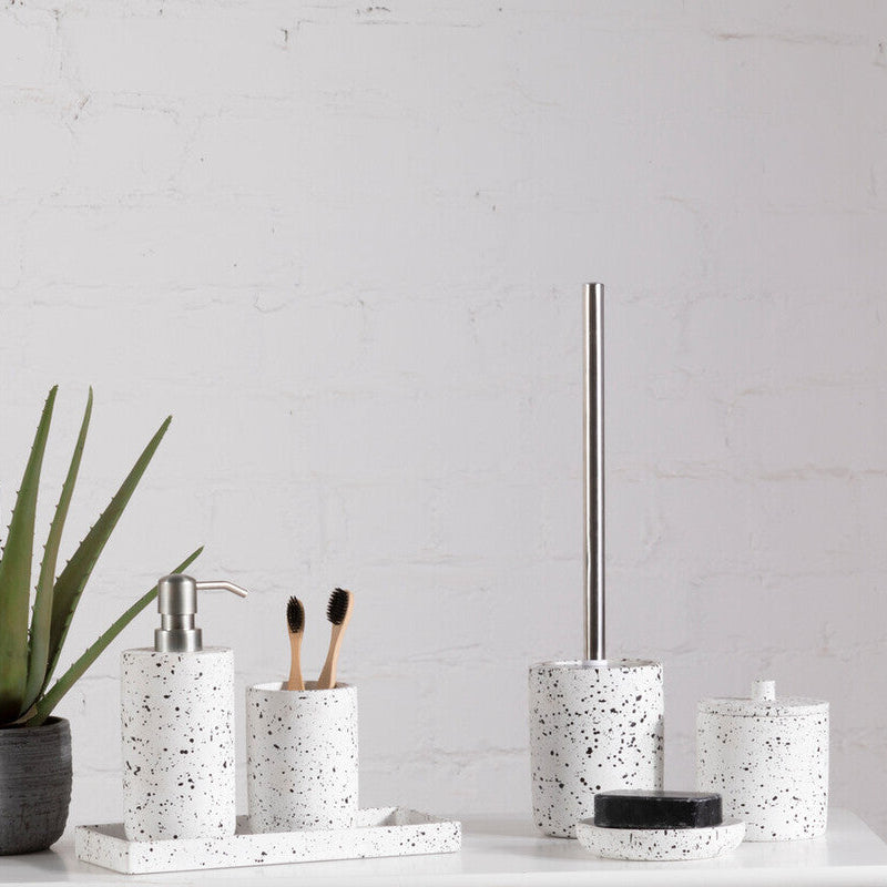 Bathroom accessories including a plant, soap dispenser, toothbrush holder, and towel rack on a white surface with a light gray wall background.