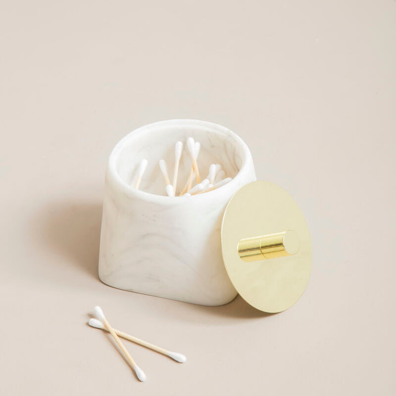 White marble container with gold lid on a beige background