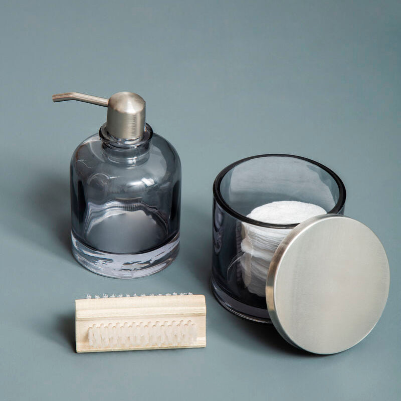 Clear glass soap dispenser, candle, and wooden block on a gray background