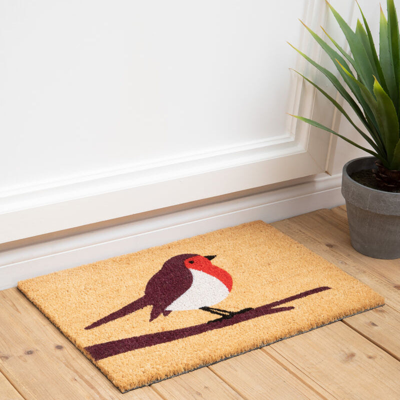 Doormat with a bird design on a wooden floor next to a plant