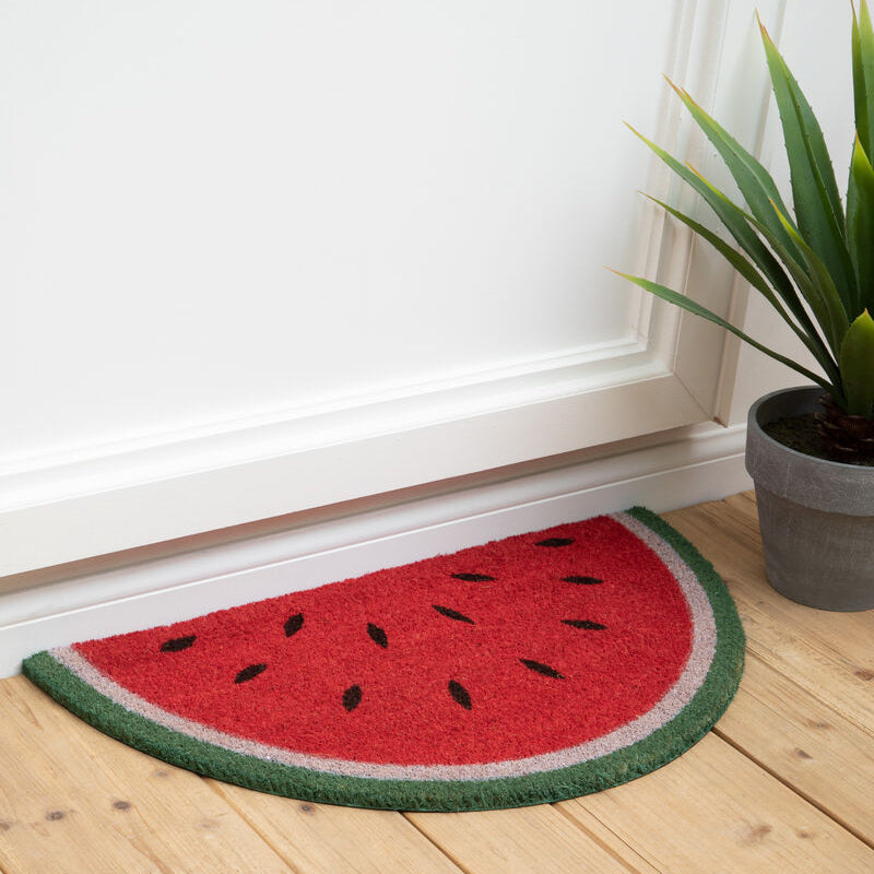 Watermelon-shaped doormat on a wooden floor with a plant in the background