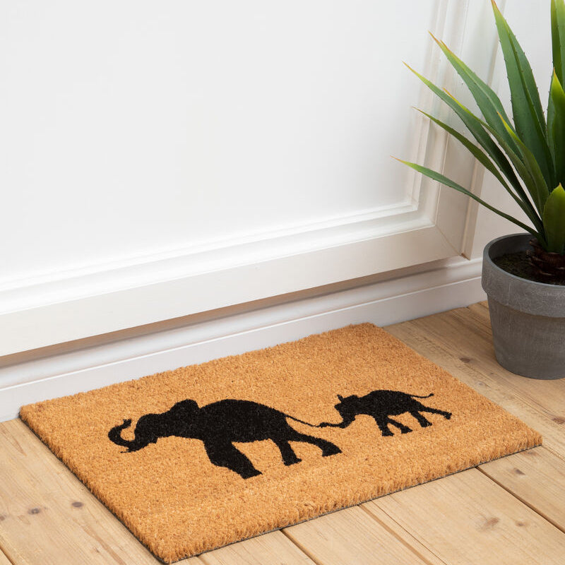 Doormat with elephant design on a wooden floor next to a plant
