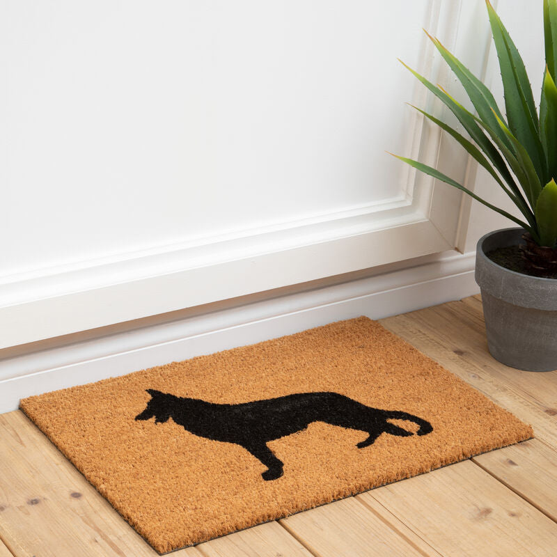 Doormat with a cat silhouette on a wooden floor next to a plant