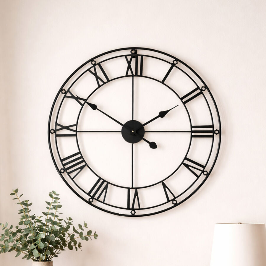 Large wall clock on a white wall with a wooden table and decorative items below.