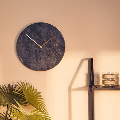 Wall clock on a beige wall with a plant and shelf in the foreground