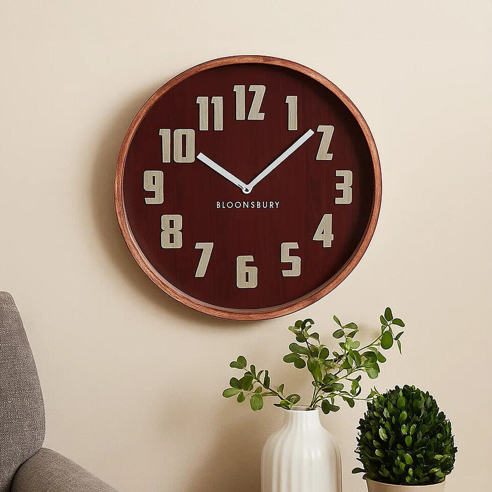 Wall clock on a beige wall above a gray armchair with a small table holding plants and a vase.