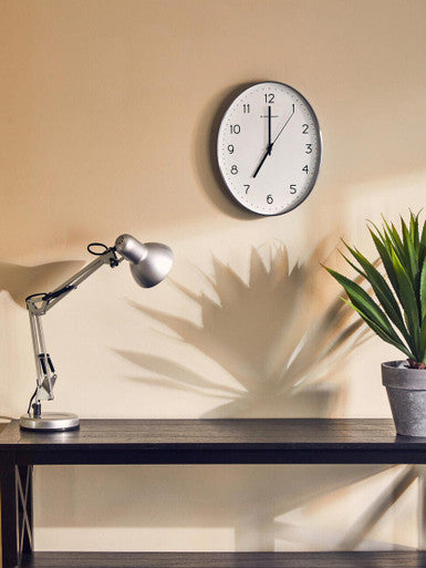 Wall clock on a beige wall above a desk with a lamp and plant