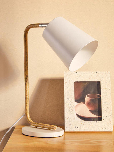 Table lamp with wooden base and white shade on a wooden surface next to a photo frame.