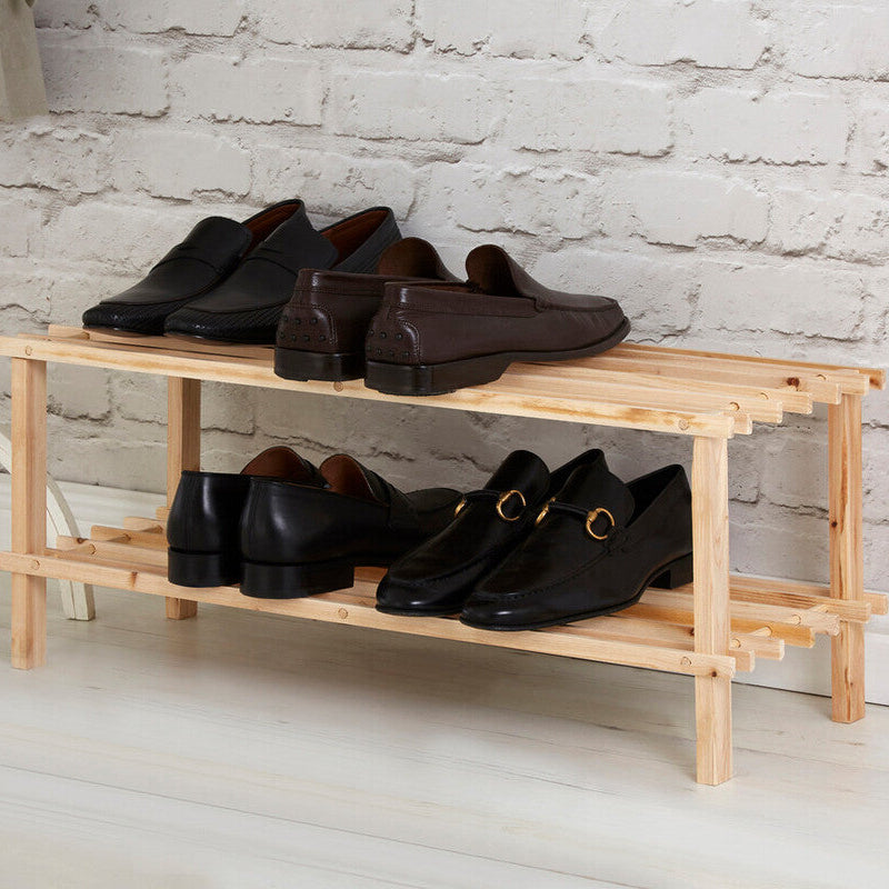 Wooden shoe rack with black shoes against a white brick wall.