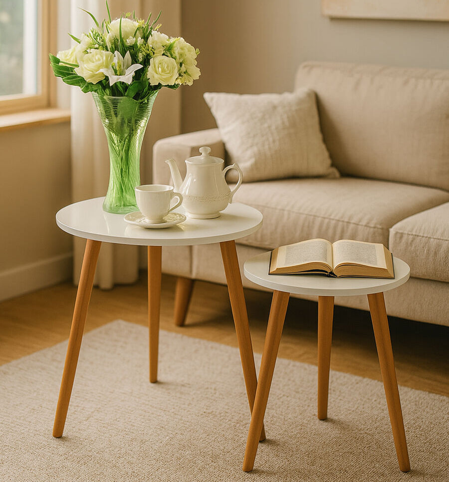 Two small round tables with a teapot, cup, and book in a living room setting.