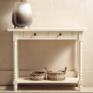 White console table with a lamp and two baskets against a beige wall.