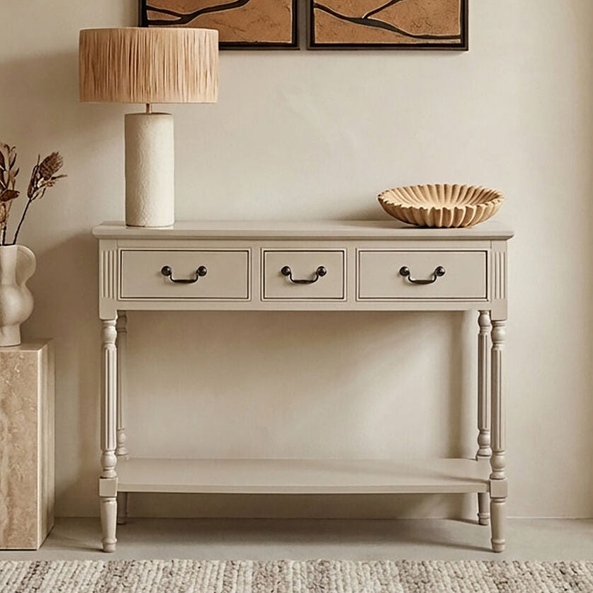 Beige console table with lamp, vase, and decorative items against a beige wall with framed artwork.