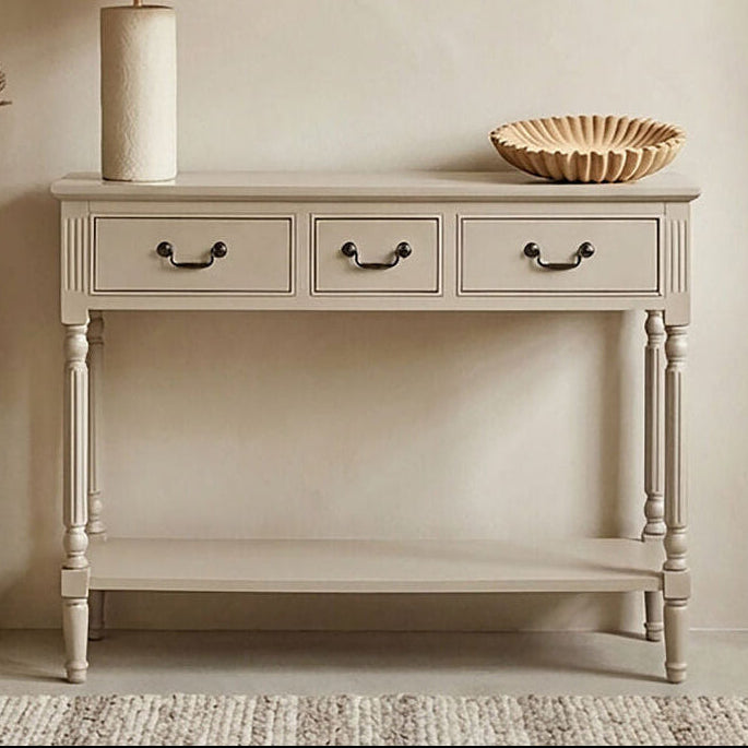 Beige console table with lamp, vase, and decorative items against a beige wall with framed artwork.