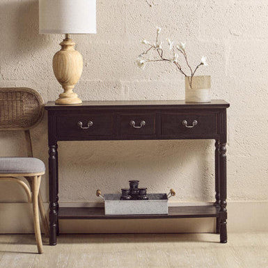 Dark wooden console table with a lamp and decorative items against a beige wall.