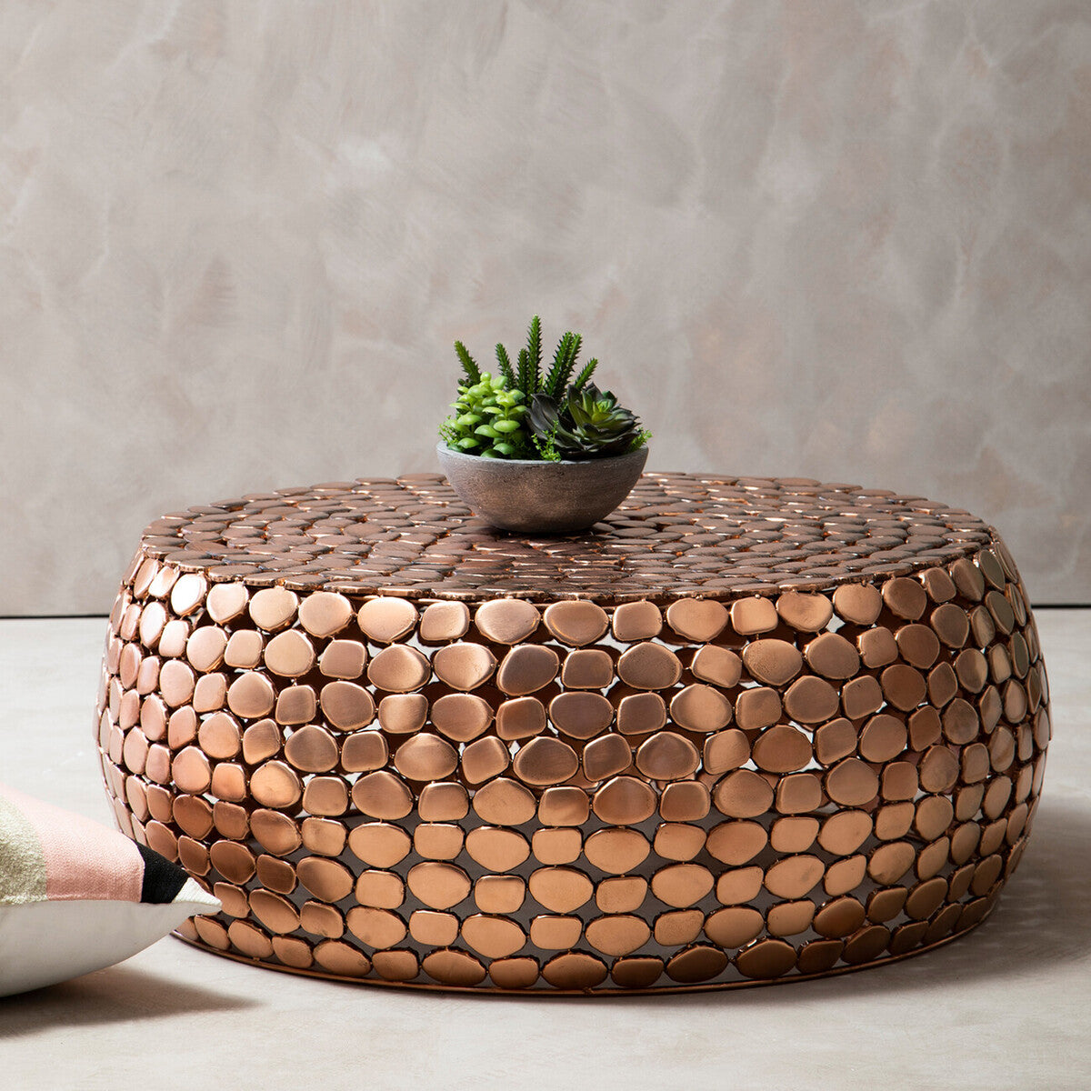 Round copper mosaic coffee table with a plant on a neutral background