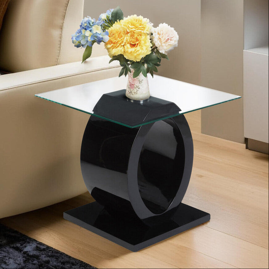 Modern black side table with a glass top displaying flowers, next to a beige sofa.
