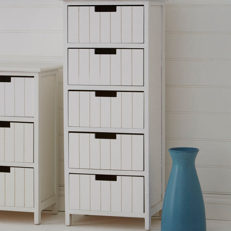 White storage cabinet with black handles next to a blue vase on a light wooden floor.