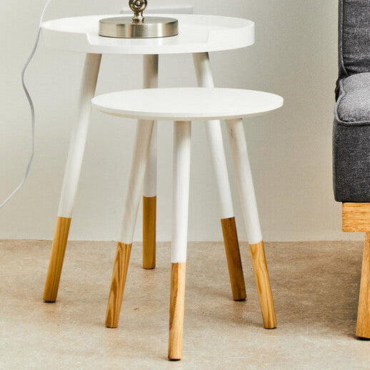 Gray sofa with a geometric-patterned pillow next to a white side table with a lamp in a minimalistic room.
