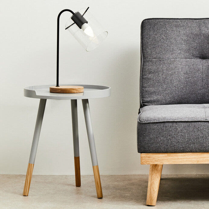 Gray sofa with a black and white pillow next to a small round table with a lamp and tray.