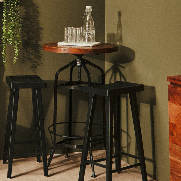 Bar area with black stools, a wooden table, and decorative items against a green wall.