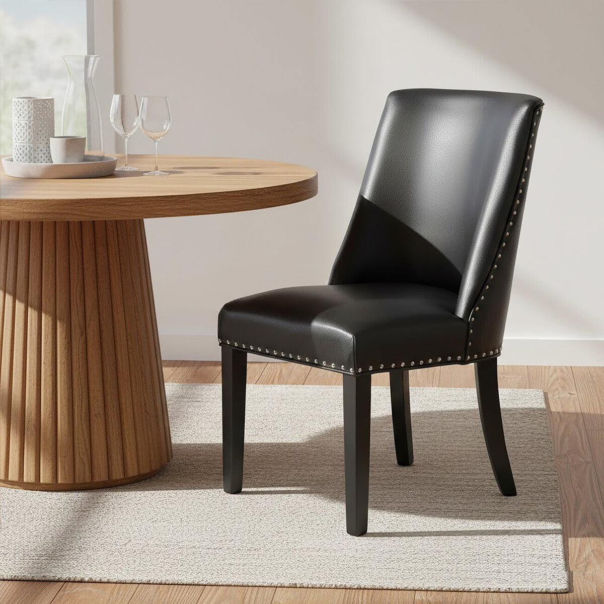Black leather chair with nailhead trim next to a wooden dining table.