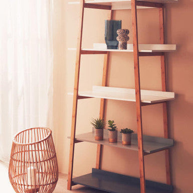 Wooden ladder shelf with white shelves against a beige wall, featuring decorative items and a woven basket.