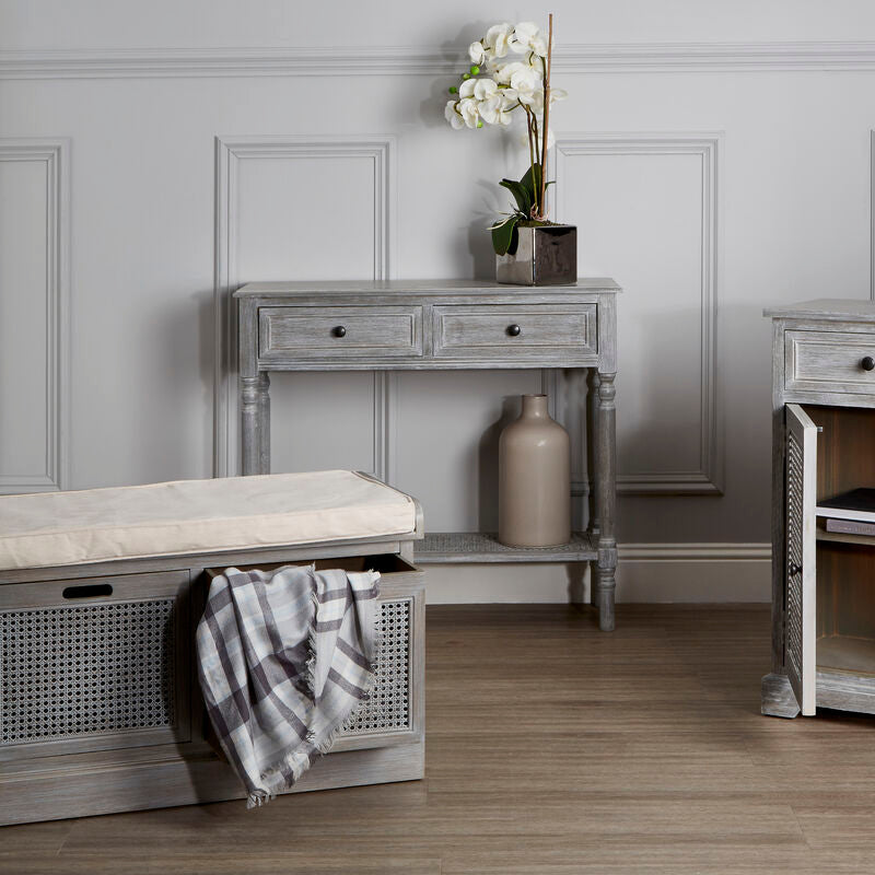 Gray wooden console table with a vase of flowers and a bench in a room with gray walls and wooden floor.