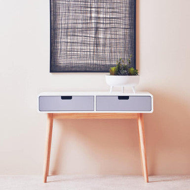 Minimalist side table with two drawers against a light wall, featuring a framed abstract artwork.