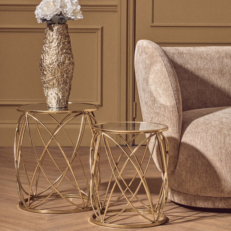 Gold side table with a vase of flowers next to a beige armchair in a room with brown walls.