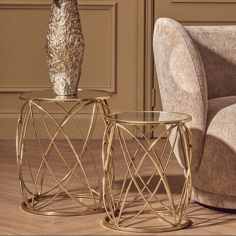 Gold side table with a vase of flowers next to a beige armchair in a room with brown walls.