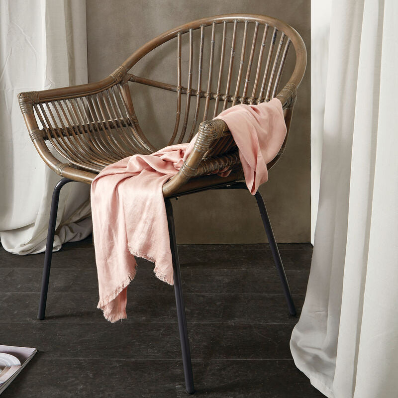 Wicker chair with a pink blanket against a neutral wall